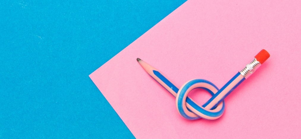 Blue pencil tied in a knot resting on a pink paper against a blue background.